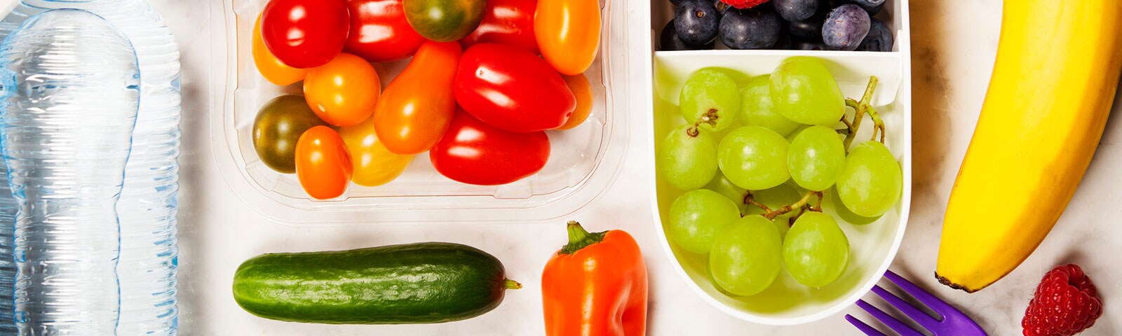 Fruits like grapes and vegetables like tomatoes in plastic containers next to a bottle of water Fruits like grapes and vegetables like tomatoes in plastic containers next to a bottle of water