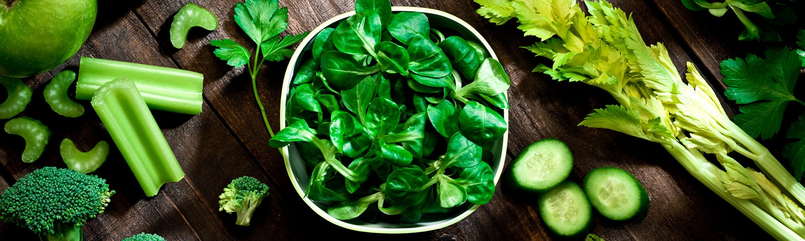 Green foods like spinach, celery, broccoli and cucumbers on a table Green foods like spinach, celery, broccoli and cucumbers on a table