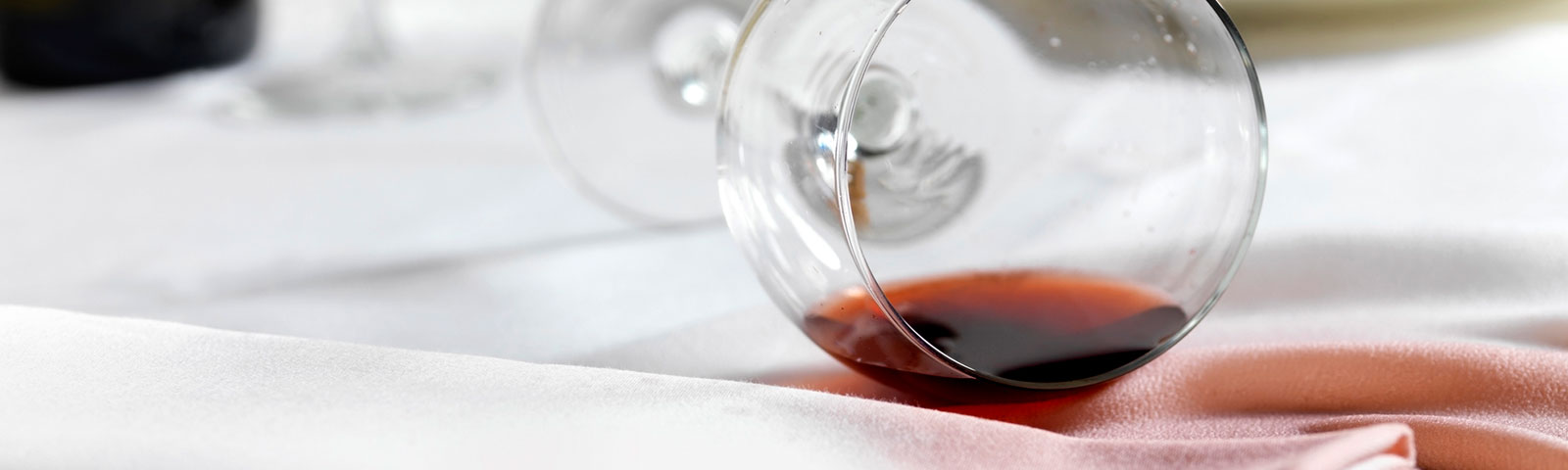 Wine glass on its side, spilling out its contents of red wine onto a white linen table cloth and creating a stain Wine glass on its side, spilling out its contents of red wine onto a white linen table cloth and creating a stain