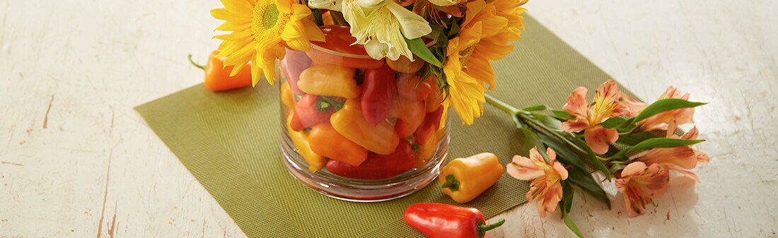 A vase full of multicolored mini peppers with sunflowers coming out of the top A vase full of multicolored mini peppers with sunflowers coming out of the top