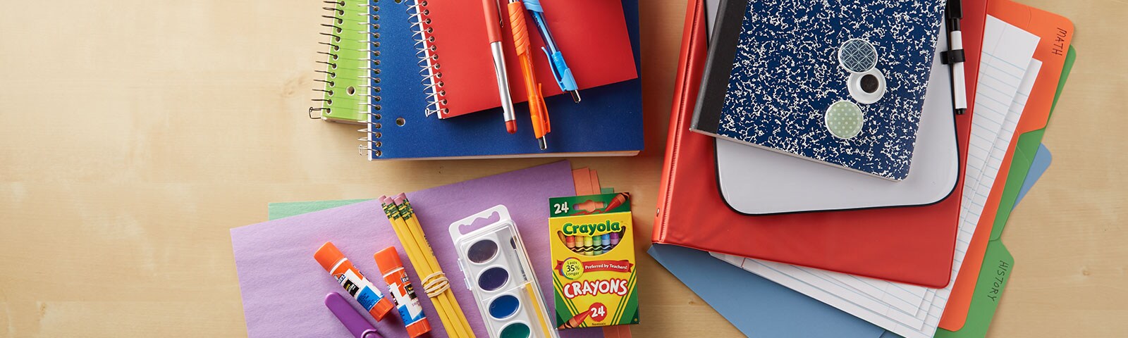 School supplies like notebooks, folders, glue sticks, pencils and pens stacked together on a table