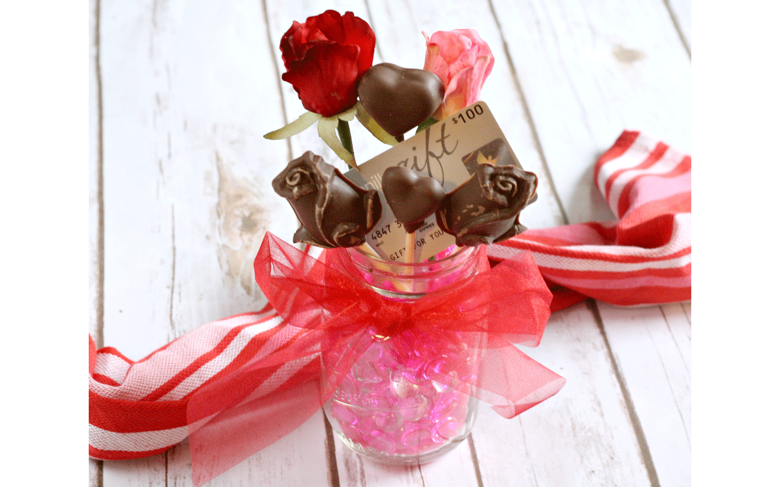 Mason jar wrapped with red ribbon tied into a bow and filled with chocolate on lollipop sticks Mason jar wrapped with red ribbon tied into a bow and filled with chocolate on lollipop sticks