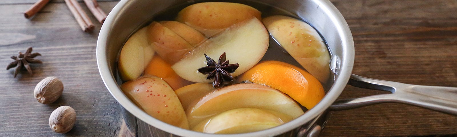A metal pot filled with water, orange and apple slices, and one star anise on a counter