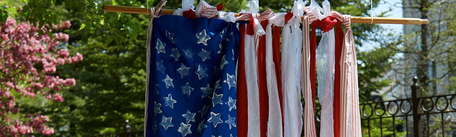 A handmade American flag hanging outside created using long strips of red and white fabric that's tied to a hanging pole A handmade American flag hanging outside created using long strips of red and white fabric that's tied to a hanging pole