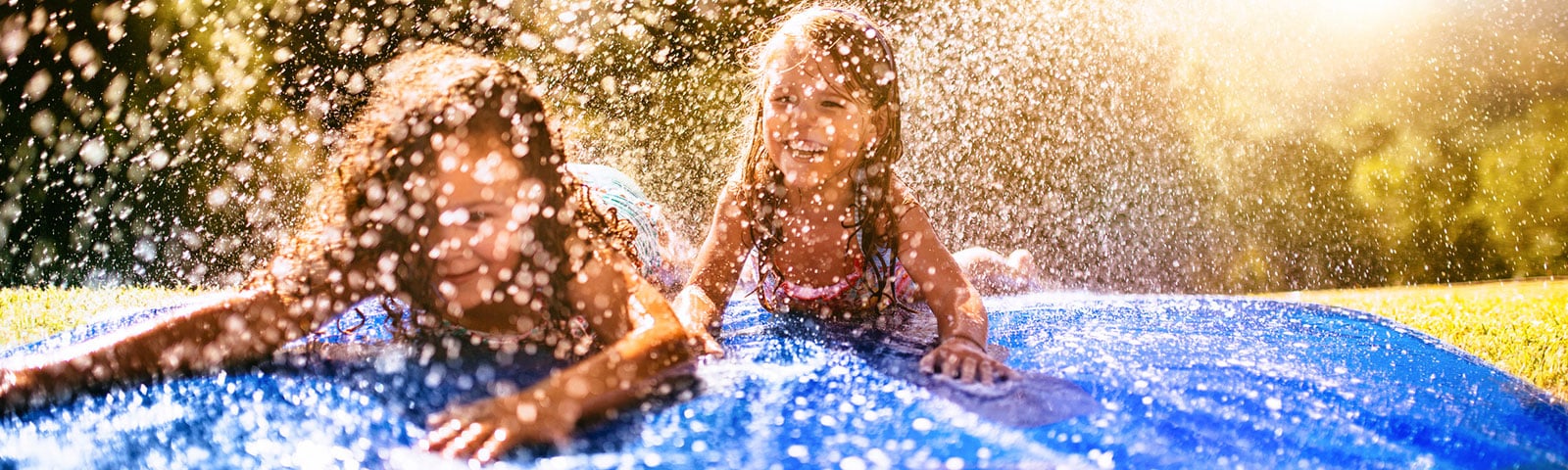 Two young children sliding head first down a slip 'n slide