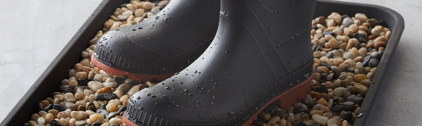 Wet rain boots atop a bed of pebbles sitting in a tray
