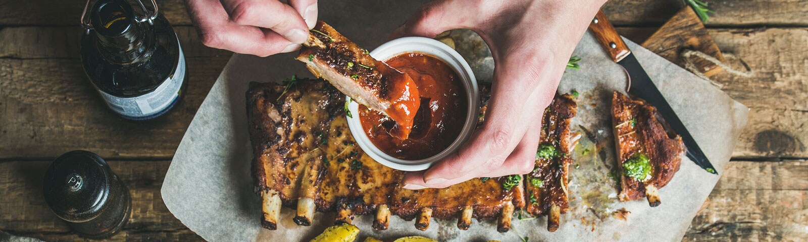 A pair of hands dipping beef ribs into barbecue sauce A pair of hands dipping beef ribs into barbecue sauce