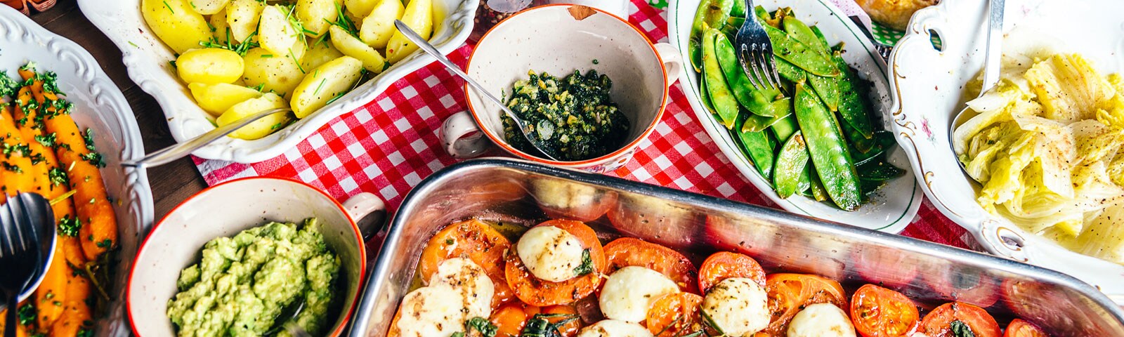 A variety of different foods in serving pans and bowls on a red gingham tablecloth